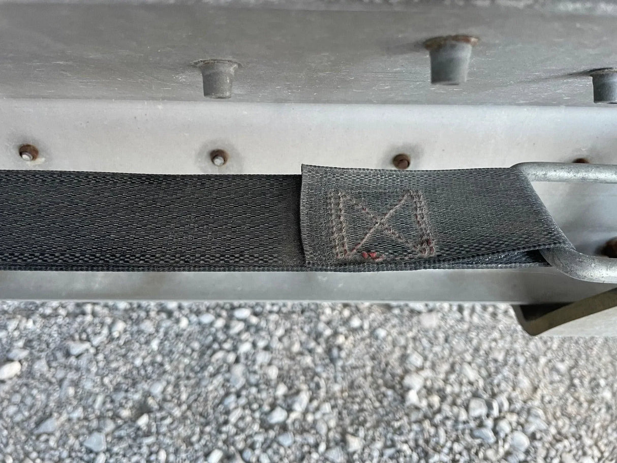 Closeup of black cargo strap with metal hook on gravel surface, heavy duty truck tie down