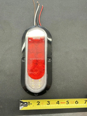 Oval LED trailer tail light with red and white lens, wires, and tape measure for scale
