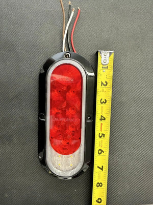 Oval LED trailer tail light with red and clear lenses next to a yellow measuring tape