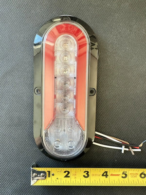 Oval LED trailer tail light with wiring, on gray surface, yellow tape measure for scale