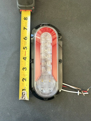 Oval LED trailer tail light with red lens, next to measuring tape showing 7 inches