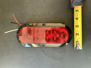 Red oval LED trailer tail light with black trim, wires exposed, next to a measuring tape