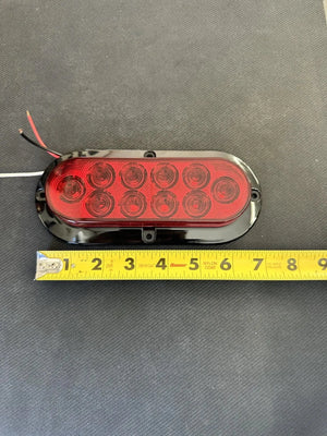 Oval red LED trailer tail light with wires, shown next to a yellow measuring tape on black surface