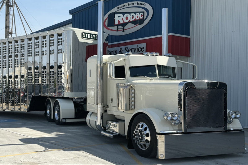 White truck with a large trailer parked in front of a building with a Rodoc logo.